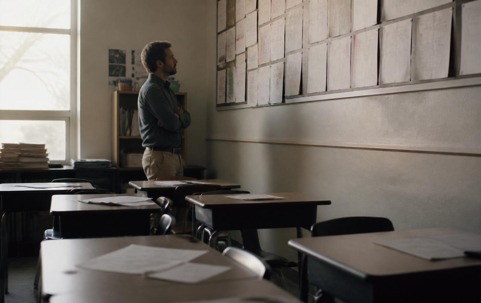 A teacher standing alone in a classroom at the end of the day, looking at a wall of student work.