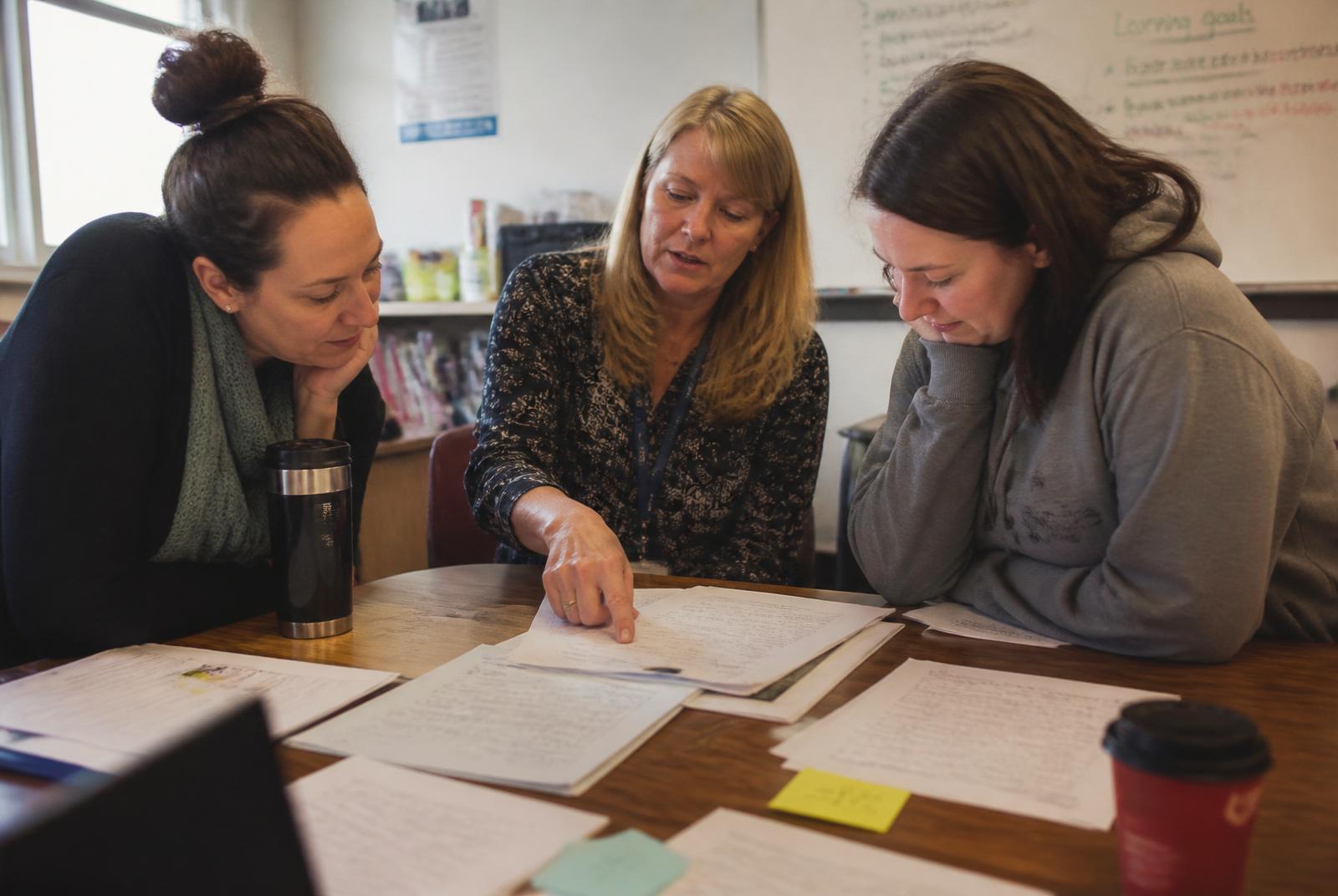 Teachers seated around a table examining the same samples of student work.